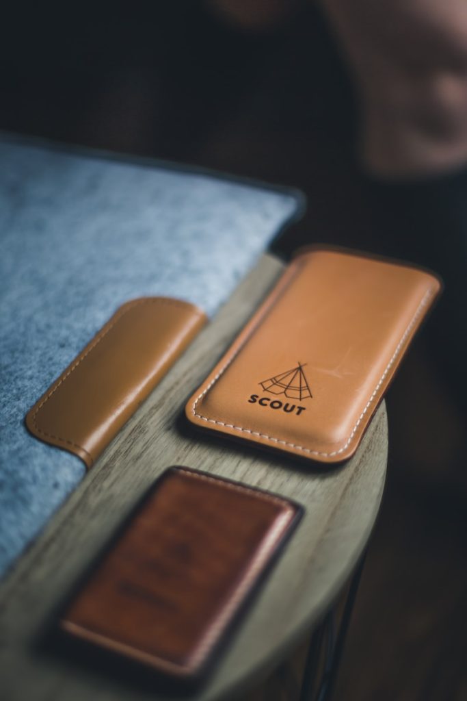 Leather laptop cover, wallet, and phone holder with a label that reads "SCOUT" on a wooden circular table