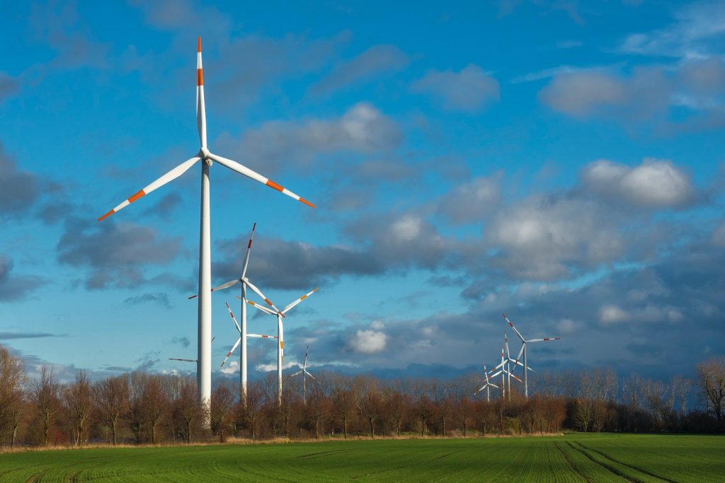 white wind turbine on green grass field under blue sky during daytime