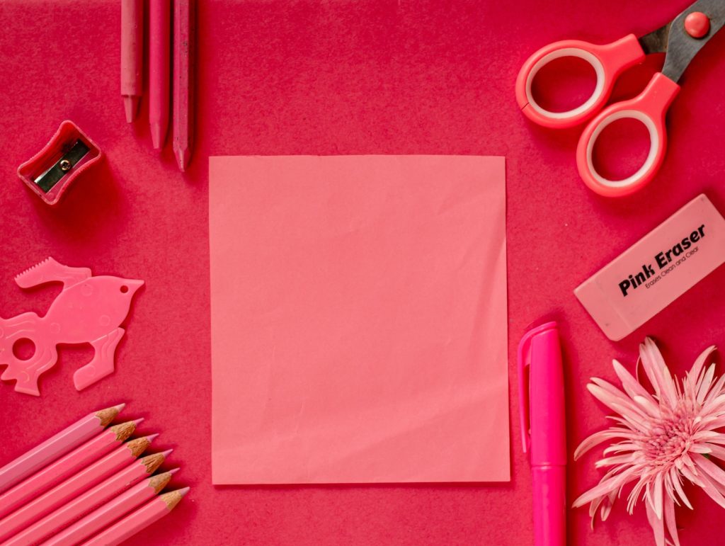 a pink desk with a notepad, pencils, scissors, and other items